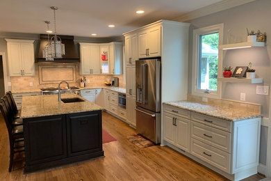 Open concept kitchen - transitional l-shaped light wood floor open concept kitchen idea in Raleigh with an undermount sink, raised-panel cabinets, white cabinets, granite countertops, beige backsplash, ceramic backsplash, stainless steel appliances, an island and beige countertops