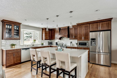 Inspiration for a mid-sized traditional u-shaped eat-in kitchen in Calgary with an undermount sink, recessed-panel cabinets, medium wood cabinets, quartzite benchtops, white splashback, subway tile splashback, stainless steel appliances, medium hardwood floors, with island, brown floor and white benchtop.