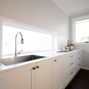 Inspiration pour une arrière-cuisine parallèle style shabby chic de taille moyenne avec un évier 2 bacs, un placard à porte shaker, des portes de placard grises, un plan de travail en surface solide, une crédence blanche, une crédence en carreau de céramique, un électroménager en acier inoxydable, un sol en bois foncé, un îlot central, un sol marron et un plan de travail blanc.