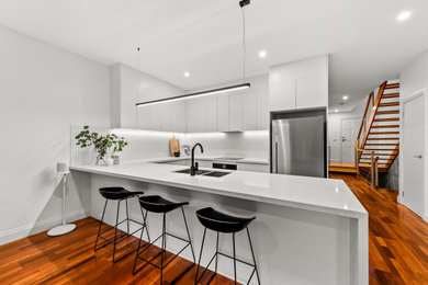 Design ideas for a mid-sized modern u-shaped open plan kitchen in Melbourne with a drop-in sink, white splashback, subway tile splashback and medium hardwood floors.
