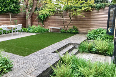 This is an example of a small contemporary back formal and private partial sun garden for summer in London with brick paving and a wood fence.