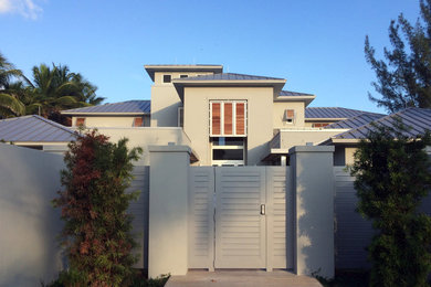Huge trendy gray two-story adobe house exterior photo in Miami with a clipped gable roof and a metal roof