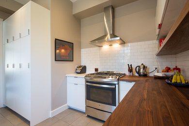 Enclosed kitchen - mid-sized scandinavian porcelain tile enclosed kitchen idea in Toronto with flat-panel cabinets, white cabinets, wood countertops, white backsplash, ceramic backsplash, stainless steel appliances and no island
