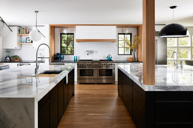 Example of a minimalist u-shaped medium tone wood floor and brown floor eat-in kitchen design in DC Metro with a drop-in sink, flat-panel cabinets, black cabinets, marble countertops, white backsplash, subway tile backsplash, stainless steel appliances and white countertops