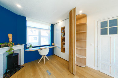 Cette photo montre un bureau de taille moyenne avec un mur bleu, parquet clair, une cheminée standard, un manteau de cheminée en pierre, un bureau intégré et un sol beige.
