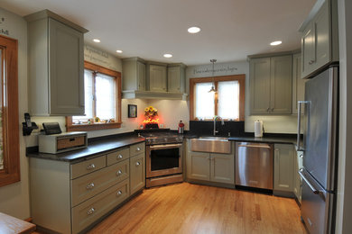 Enclosed kitchen - mid-sized transitional u-shaped light wood floor enclosed kitchen idea in Milwaukee with a farmhouse sink, flat-panel cabinets, green cabinets, granite countertops, stainless steel appliances and no island