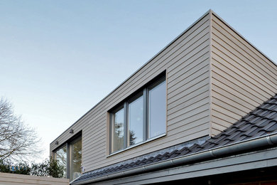 Photo of a contemporary grey house exterior in Hamburg with wood siding, a gable roof and a tile roof.