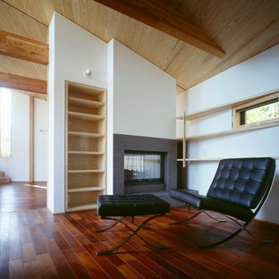 Inspiration for a medium sized modern home office and library in Other with a reading nook, white walls, dark hardwood flooring, a two-sided fireplace, a stone fireplace surround and red floors.