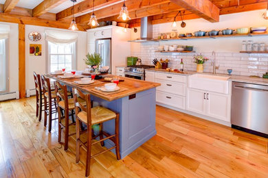 Example of a mid-sized cottage light wood floor and brown floor eat-in kitchen design in Boston with a farmhouse sink, shaker cabinets, white cabinets, granite countertops, white backsplash, porcelain backsplash, stainless steel appliances, an island and gray countertops
