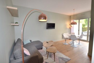 This is an example of a small contemporary open plan games room in Lille with green walls, light hardwood flooring, a wall mounted tv and beige floors.