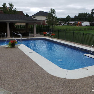 Bild på en stor l-formad pool på baksidan av huset, med betongplatta