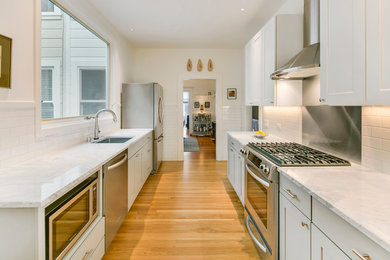Small contemporary galley separate kitchen in San Francisco with recessed-panel cabinets, grey cabinets, marble benchtops, a single-bowl sink, white splashback, subway tile splashback, stainless steel appliances, light hardwood floors, no island, brown floor and grey benchtop.