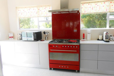 Inspiration for a mid-sized modern l-shaped porcelain tile eat-in kitchen remodel in Other with a farmhouse sink, flat-panel cabinets, gray cabinets, granite countertops, red backsplash, stone slab backsplash, colored appliances and no island
