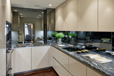 Design ideas for an u-shaped enclosed kitchen in London with a built-in sink, flat-panel cabinets, beige cabinets, granite worktops, black splashback, mirror splashback, stainless steel appliances, medium hardwood flooring, no island, brown floors and black worktops.