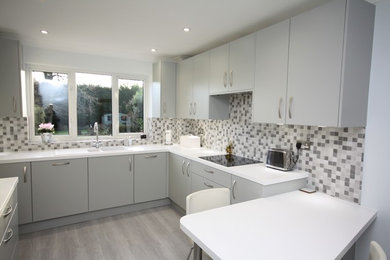 This is an example of a contemporary kitchen in Essex with flat-panel cabinets, grey cabinets and a breakfast bar.