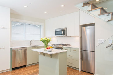 Photo of a small midcentury l-shaped kitchen in Vancouver with flat-panel cabinets, white cabinets, stainless steel appliances, light hardwood floors, with island and brown floor.