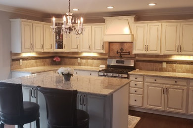 Photo of a large u-shaped eat-in kitchen in Detroit with an undermount sink, recessed-panel cabinets, white cabinets, granite benchtops, beige splashback, limestone splashback, stainless steel appliances, dark hardwood floors, with island, brown floor and multi-coloured benchtop.