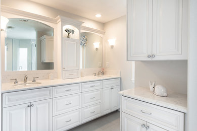 This is an example of a mid-sized traditional master bathroom in Los Angeles with raised-panel cabinets, white cabinets, a drop-in tub, a corner shower, a two-piece toilet, white tile, porcelain tile, grey walls, porcelain floors, an undermount sink, engineered quartz benchtops, grey floor and a hinged shower door.