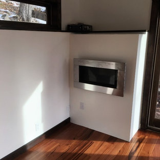 ニューヨークの中サイズのモダンスタイルのおしゃれなアトリエ・スタジオ (ベージュの壁、無垢フローリング、吊り下げ式暖炉、金属の暖炉まわり、造り付け机) の写真