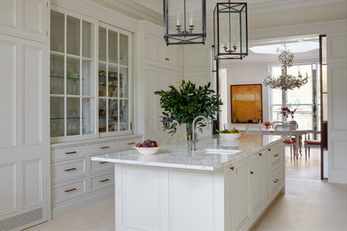 Photo of a large traditional galley eat-in kitchen in London with a double-bowl sink, recessed-panel cabinets, white cabinets, marble benchtops, white splashback, marble splashback, white appliances, limestone floors, with island, beige floor and white benchtop.