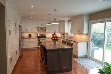 Large transitional u-shaped separate kitchen in Toronto with shaker cabinets, white cabinets, granite benchtops, beige splashback, ceramic splashback, stainless steel appliances, medium hardwood floors, with island, a double-bowl sink and brown floor.