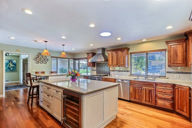 Inspiration for a mid-sized transitional l-shaped light wood floor eat-in kitchen remodel in San Francisco with an undermount sink, raised-panel cabinets, medium tone wood cabinets, granite countertops, white backsplash, ceramic backsplash, stainless steel appliances and an island