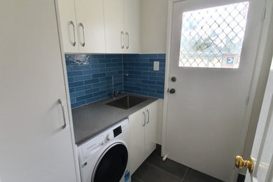 Photo of a mid-sized contemporary single-wall dedicated laundry room in Sydney with an integrated sink, flat-panel cabinets, white cabinets, quartz benchtops, blue splashback, matchstick tile splashback, white walls, ceramic floors, a side-by-side washer and dryer, grey floor and grey benchtop.