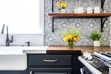 Mid-sized farmhouse l-shaped laminate floor and brown floor open concept kitchen photo in Los Angeles with a farmhouse sink, raised-panel cabinets, blue cabinets, wood countertops, blue backsplash, cement tile backsplash, stainless steel appliances, an island and brown countertops