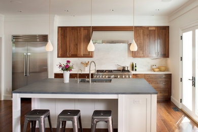 Kitchen - large transitional single-wall medium tone wood floor kitchen idea in Boston with a double-bowl sink, shaker cabinets, medium tone wood cabinets, marble countertops, white backsplash, stone slab backsplash, stainless steel appliances and an island