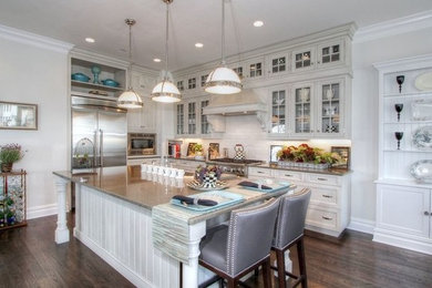 Inspiration for a l-shaped dark wood floor and brown floor eat-in kitchen remodel in Philadelphia with a farmhouse sink, glass-front cabinets, beige cabinets, granite countertops, white backsplash, subway tile backsplash, stainless steel appliances and an island
