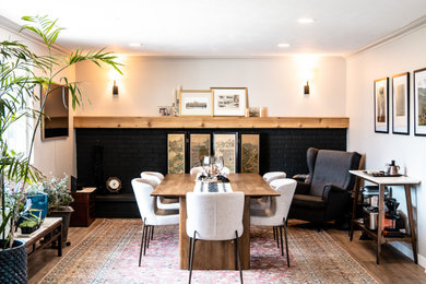 Immagine di una sala da pranzo aperta verso la cucina classica di medie dimensioni con pareti bianche, pavimento in legno massello medio, camino classico e cornice del camino in mattoni