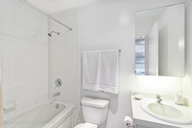 Design ideas for a mid-sized contemporary 3/4 bathroom in Toronto with a drop-in sink, flat-panel cabinets, white cabinets, solid surface benchtops, an alcove tub, a shower/bathtub combo, a two-piece toilet, white tile, subway tile, white walls and porcelain floors.