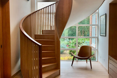Ejemplo de escalera curva contemporánea grande con escalones de madera, contrahuellas de madera y barandilla de madera