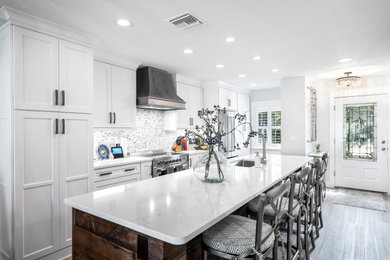 Example of a mid-sized eclectic galley vinyl floor and brown floor open concept kitchen design in Tampa with an undermount sink, shaker cabinets, white cabinets, quartz countertops, gray backsplash, porcelain backsplash, stainless steel appliances, an island and white countertops