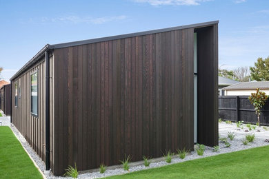Mid-sized contemporary one-storey black house exterior in Christchurch with wood siding, a flat roof and a metal roof.
