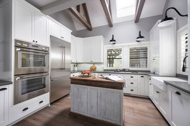 Example of a mid-sized farmhouse u-shaped medium tone wood floor, gray floor and exposed beam eat-in kitchen design in Other with a farmhouse sink, shaker cabinets, white cabinets, quartz countertops, gray backsplash, porcelain backsplash, stainless steel appliances, an island and gray countertops