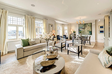 This is an example of a large contemporary open plan living room in London with white walls, light hardwood flooring, a concealed tv and beige floors.