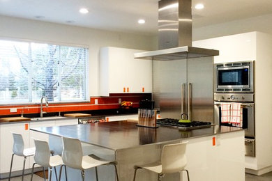 Inspiration for a mid-sized modern l-shaped ceramic tile eat-in kitchen remodel in Other with an undermount sink, flat-panel cabinets, white cabinets, stainless steel countertops, orange backsplash, glass tile backsplash, stainless steel appliances and an island
