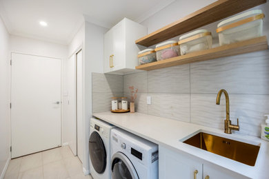 Photo of a small modern single-wall separated utility room in Auckland with a single-bowl sink, shaker cabinets, white cabinets, engineered stone countertops, white splashback, ceramic splashback, white walls, porcelain flooring, a side by side washer and dryer, grey floors and white worktops.