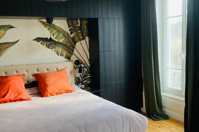 Modelo de dormitorio principal y beige y blanco tropical grande sin chimenea con paredes beige, suelo de madera clara y papel pintado