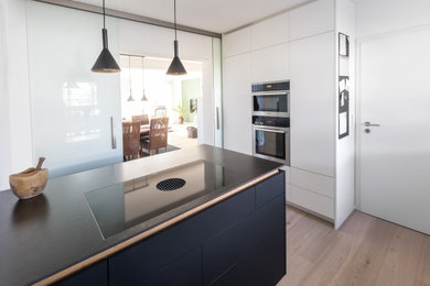 Geschlossene, Zweizeilige, Mittelgroße Moderne Küche mit weißen Schränken, Küchenrückwand in Weiß, hellem Holzboden, Kücheninsel und schwarzer Arbeitsplatte in Stuttgart