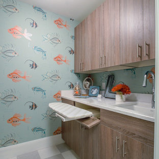 ミネアポリスの中サイズのビーチスタイルのおしゃれな洗濯室 (アンダーカウンターシンク、フラットパネル扉のキャビネット、大理石カウンター、青い壁、リノリウムの床、上下配置の洗濯機・乾燥機、中間色木目調キャビネット) の写真