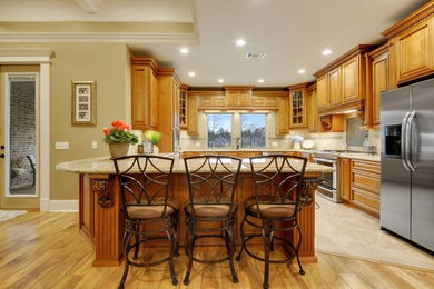 Example of a mid-sized classic kitchen design in New Orleans with a drop-in sink, raised-panel cabinets, light wood cabinets, beige backsplash, stainless steel appliances and an island