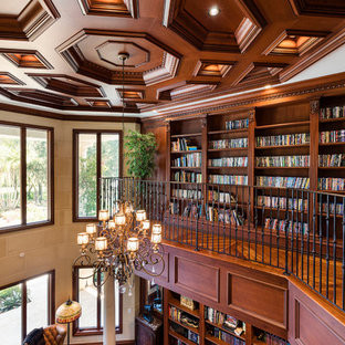 Foto di un ampio studio mediterraneo con libreria, pareti beige, pavimento in legno massello medio, camino classico, cornice del camino in pietra, scrivania autoportante e pavimento marrone