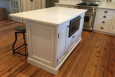 Example of a mid-sized arts and crafts l-shaped medium tone wood floor and brown floor kitchen design in Charlotte with shaker cabinets, white cabinets, quartz countertops, white backsplash, ceramic backsplash, stainless steel appliances, an island and white countertops