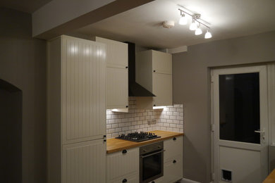 This is an example of a contemporary kitchen in London with raised-panel cabinets, beige cabinets, laminate countertops, white splashback, ceramic splashback, stainless steel appliances and dark hardwood flooring.