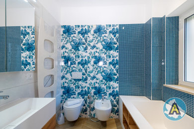 Foto di una piccola stanza da bagno minimal con ante lisce, ante in legno chiaro, vasca freestanding, WC sospeso, piastrelle blu, piastrelle a mosaico, pavimento in gres porcellanato, top in superficie solida, un lavabo e mobile bagno sospeso
