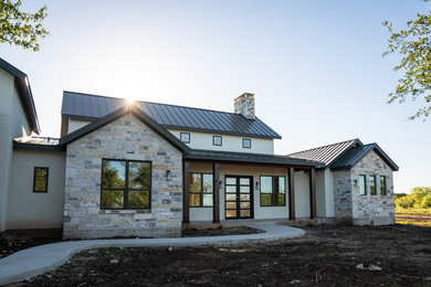 Inspiration for a large country white two-story stucco house exterior remodel in Austin with a hip roof and a metal roof