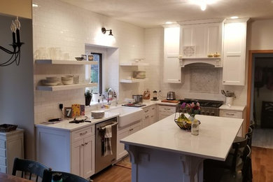 Mid-sized u-shaped medium tone wood floor and brown floor eat-in kitchen photo in Omaha with a farmhouse sink, flat-panel cabinets, white cabinets, quartz countertops, white backsplash, stainless steel appliances, an island and white countertops