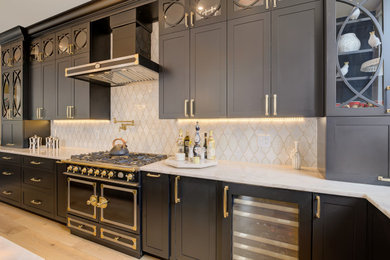 Photo of a large transitional l-shaped eat-in kitchen in Philadelphia with an undermount sink, recessed-panel cabinets, black cabinets, quartz benchtops, white splashback, porcelain splashback, black appliances, light hardwood floors, with island, brown floor and white benchtop.